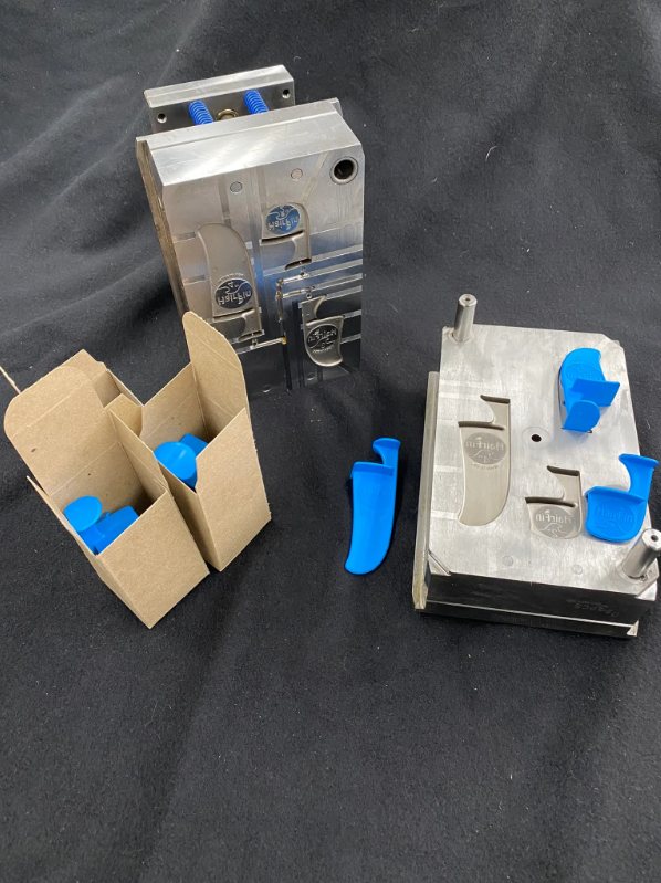 A two-plate mold beside finished blue molded parts packed in cartons