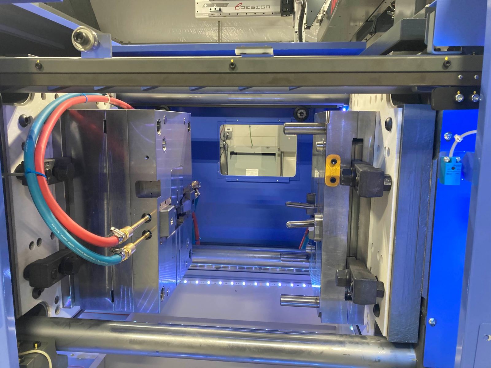 An open injection mold mounted in a press, with water lines connected